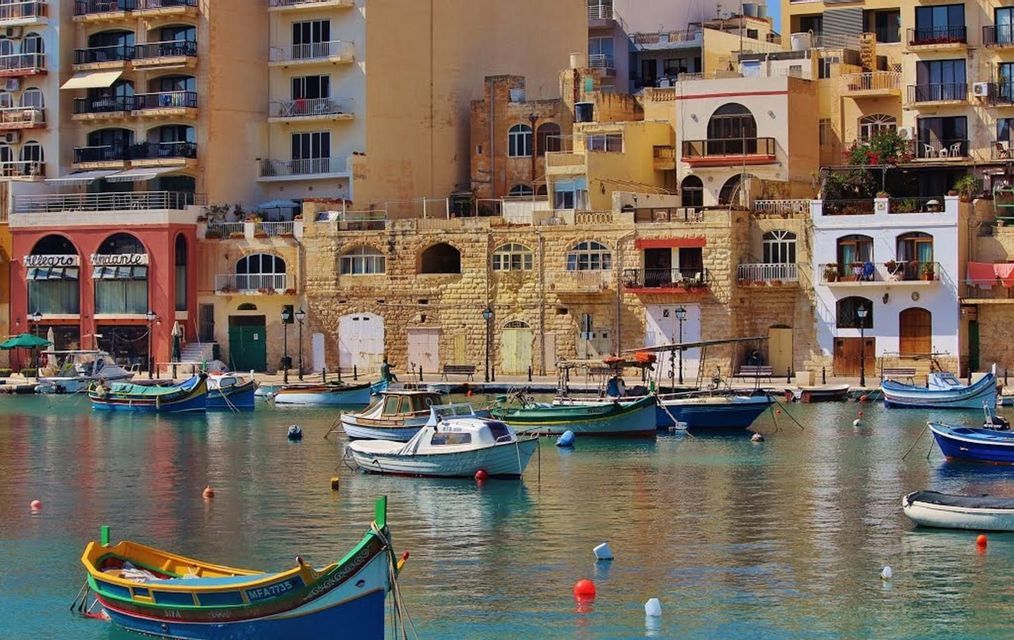 Barcos coloridos amarrados en un puerto tranquilo con edificios tradicionales de piedra amarilla a lo largo del muelle.