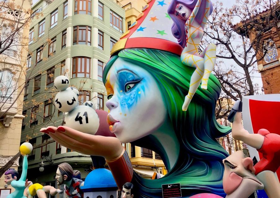 Una grande e colorata scultura di una donna con i capelli verdi che soffia palline della lotteria dalla mano in una strada cittadina.