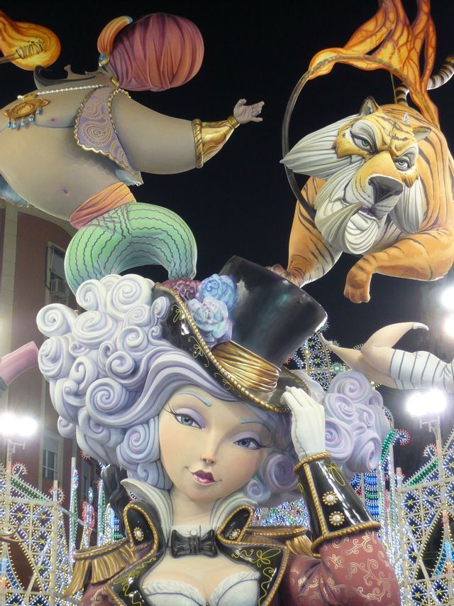 Grandi sculture colorate di una donna con cilindro, una tigre e un genio illuminate contro un cielo notturno scuro.