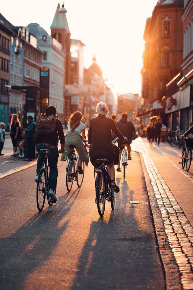 Un gruppo WeRoad in bicicletta percorre una strada cittadina in ciottoli al tramonto, proiettando lunghe ombre sulla strada.