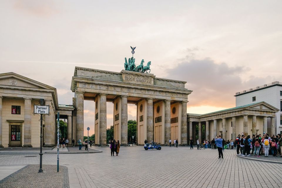 Un gruppo WeRoad e altre persone si radunano in una grande piazza lastricata di fronte a un monumentale arco neoclassico al tramonto.