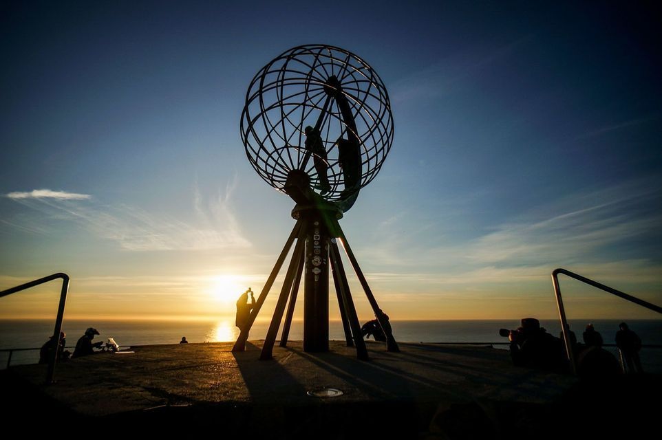 Un viaje en grupo de WeRoad silueteado al atardecer junto a una enorme escultura de globo con vistas al océano.