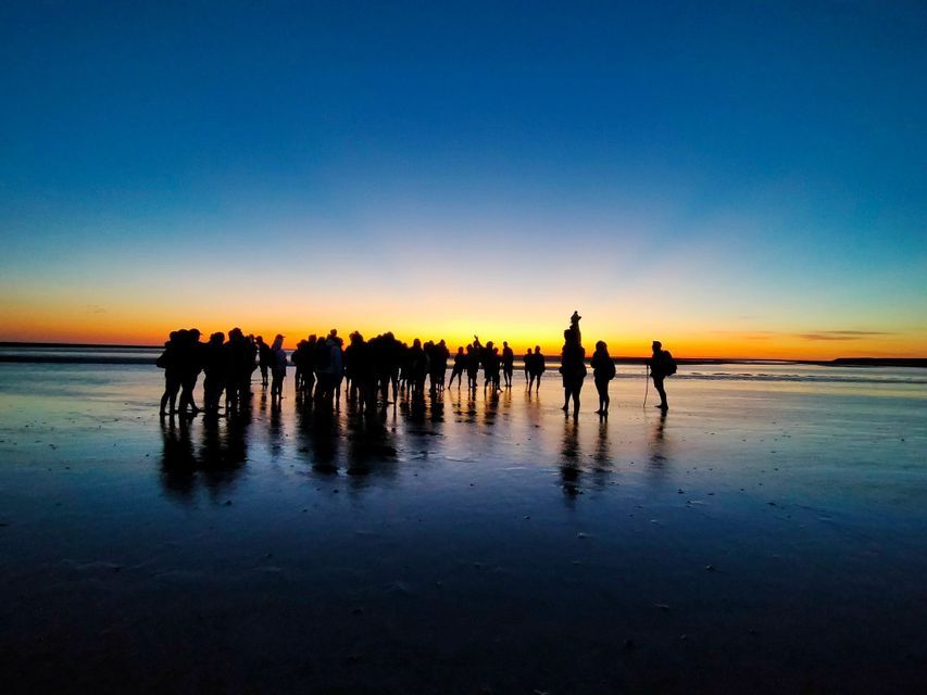 Un viaje en grupo de WeRoad silueteado contra un atardecer en una playa mojada, con sus reflejos en la arena.