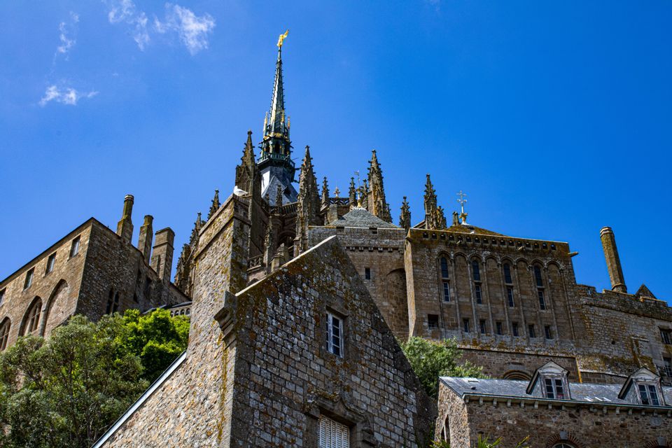 Vue en contre-plongée d'une abbaye gothique historique avec une haute flèche centrale s'élançant vers un ciel bleu éclatant.
