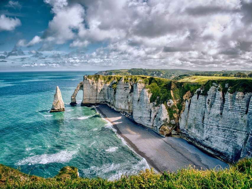 Falaises de craie blanche avec une arche naturelle et une cheminée, le long d&#39;une côte aux eaux turquoise sous un ciel nuageux.