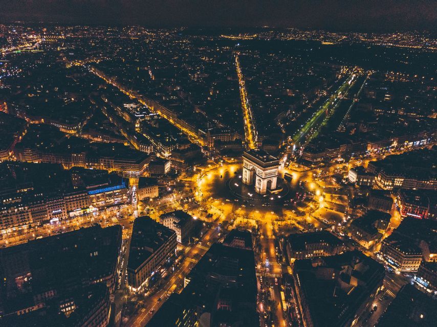 Vue aérienne d&#39;une arche monumentale illuminée au centre d&#39;un rond-point, avec les rues de la ville rayonnant la nuit.