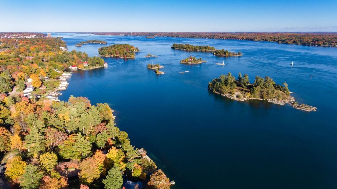 An aerial view of numerous islands covered in colorful autumn trees scattered across a deep blue body of water.