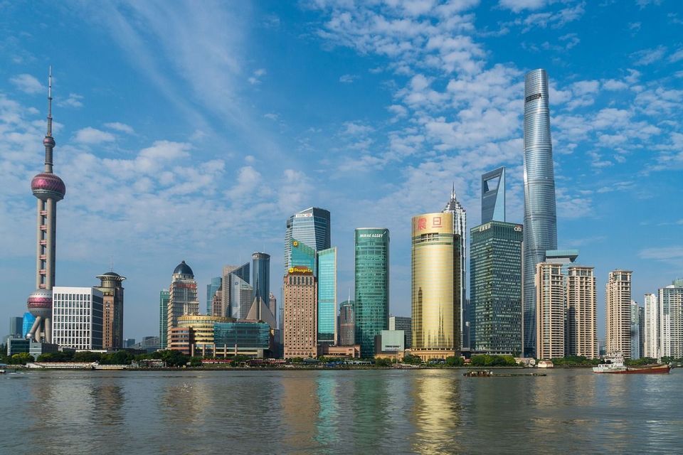 Lo skyline moderno di una città con numerosi grattacieli, visto dalla sponda opposta di un fiume sotto un cielo azzurro con nuvole leggere.