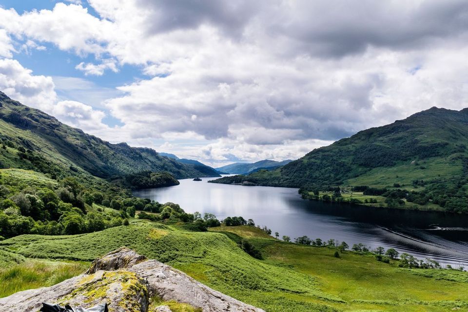 Una vista panorámica de un lago sereno enclavado entre exuberantes montañas verdes bajo un cielo con nubes blancas y grises.