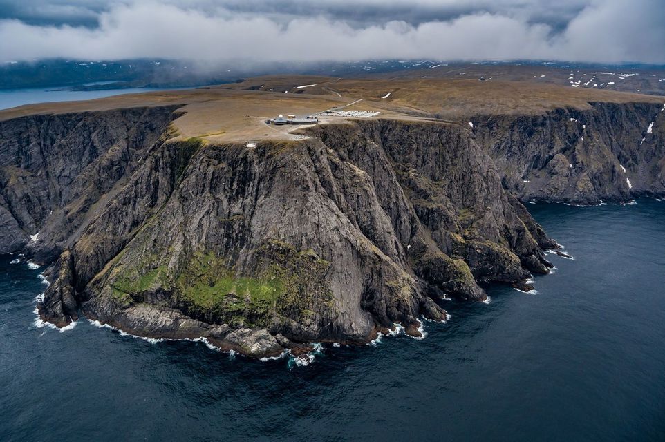 Un complesso di edifici sorge su un'ampia scogliera rocciosa che si protende nell'oceano scuro sotto un cielo coperto.