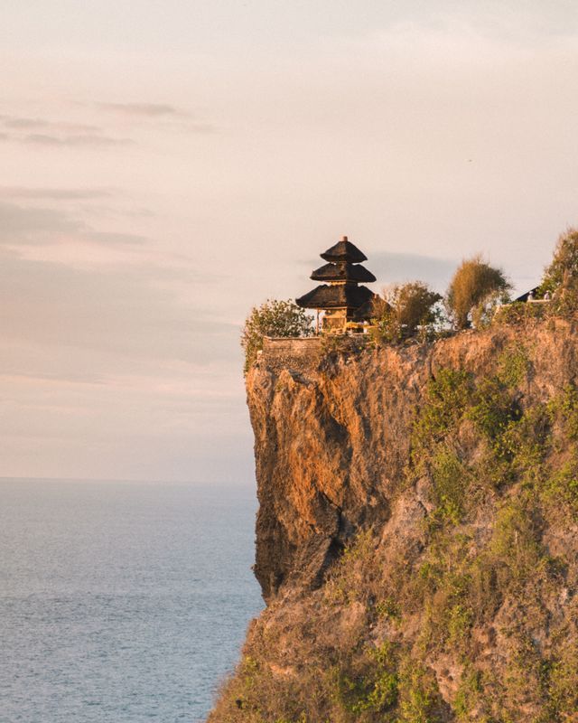 Un tempio in stile pagoda, con tetto a gradoni, si erge su un'alta scogliera rocciosa che domina l'oceano al tramonto.