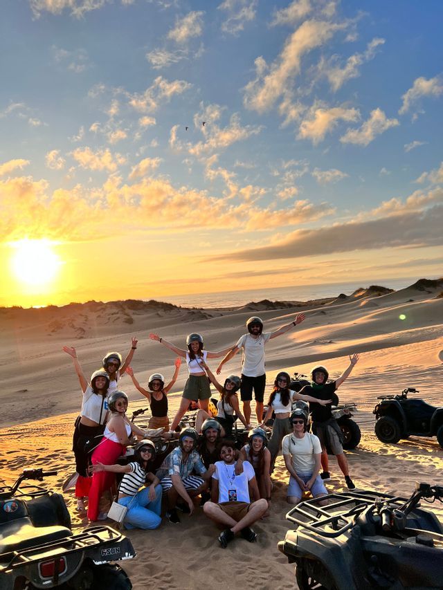 Un gruppo WeRoad in posa con i quad sulle dune di sabbia sotto un tramonto dorato.