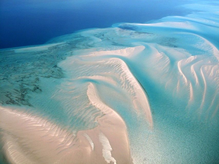 Vista aerea di banchi di sabbia bianchi in acque turchesi e poco profonde, che si fondono con la profonda distesa blu dell'oceano.