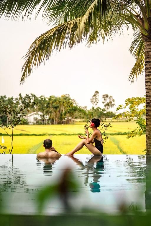 Un homme et une femme participant à un voyage de groupe WeRoad se détendent dans une piscine à débordement, surplombant une rizière d'un jaune éclatant.