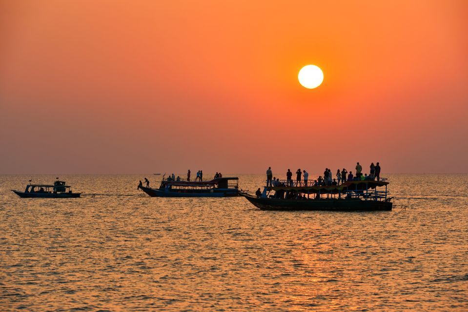 Un groupe WeRoad en silhouette sur des bateaux, admirant le coucher de soleil sur l'eau.