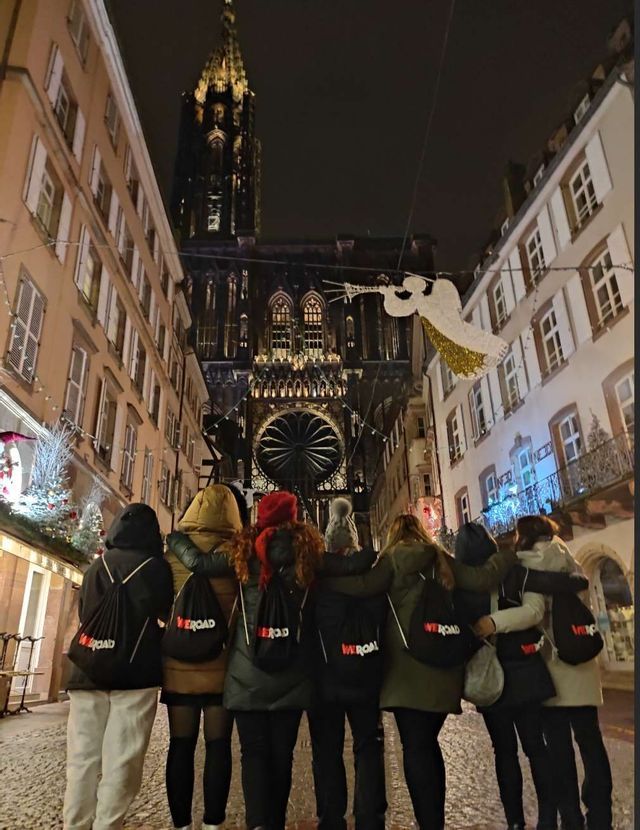 Eine WeRoad-Reisegruppe steht nachts auf einer Straße vor einer beleuchteten gotischen Kathedrale mit Weihnachtsdekoration.