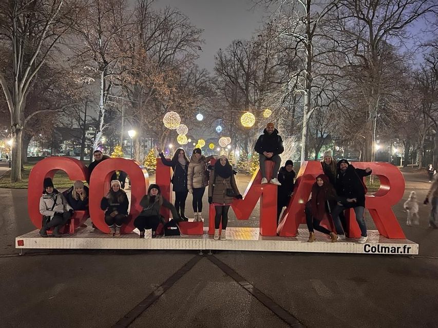 Un gruppo WeRoad si fa fotografare tra e intorno a grandi lettere rosse in un parco notturno, illuminate da luci festive.