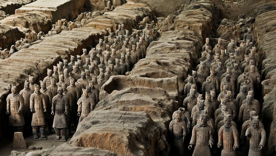 Panoramica dall'alto di centinaia di statue di soldati di terracotta disposte in formazione all'interno di fosse di scavo.