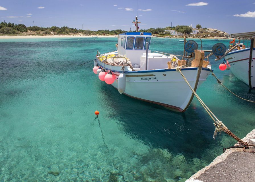 Una barca da pesca bianca con boe rosa ormeggiata in acqua cristallina turchese vicino a un molo in una giornata di sole.