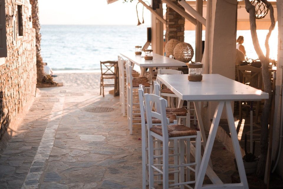 Una fila di tavoli alti bianchi e sedie in un vicoletto in pietra di un bar sul mare con vista sull'oceano