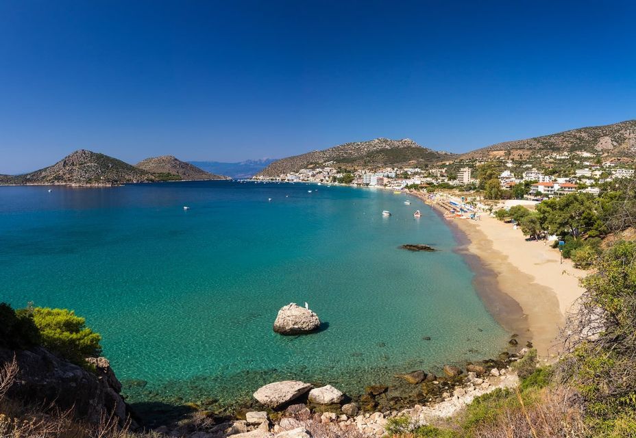 Una vista dall'alto di una spiaggia sabbiosa e di una città costiera che si affaccia su una baia di acqua cristallina e turchese, con colline sullo sfondo.