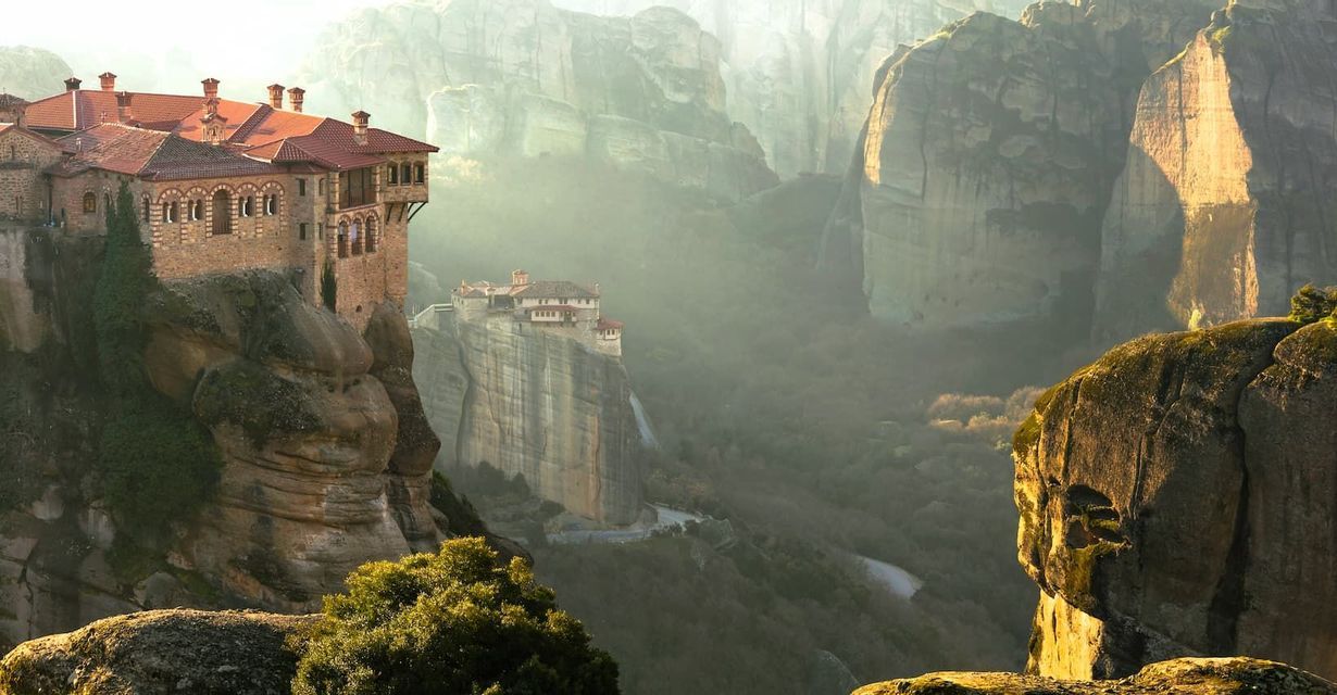 Antichi monasteri dai tetti rossi, arroccati su imponenti formazioni rocciose in una valle nebbiosa e baciata dal sole.