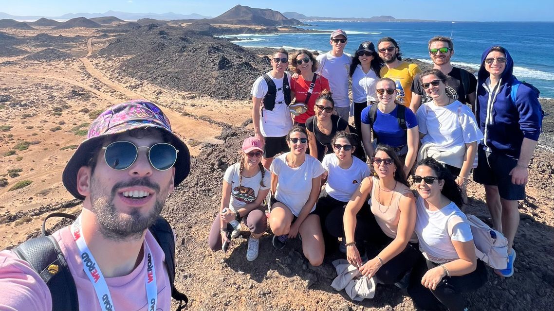 Un viaje en grupo de WeRoad se toma una selfie en una colina rocosa con vistas a una costa soleada y el océano.