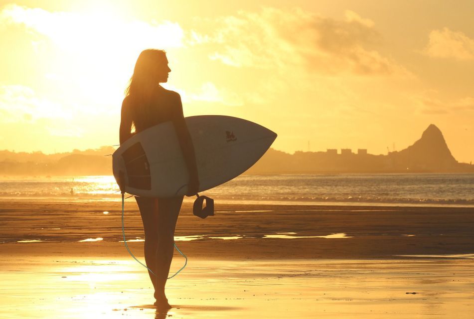Una donna in silhouette tiene una tavola da surf su una spiaggia al tramonto, guardando verso l'oceano.