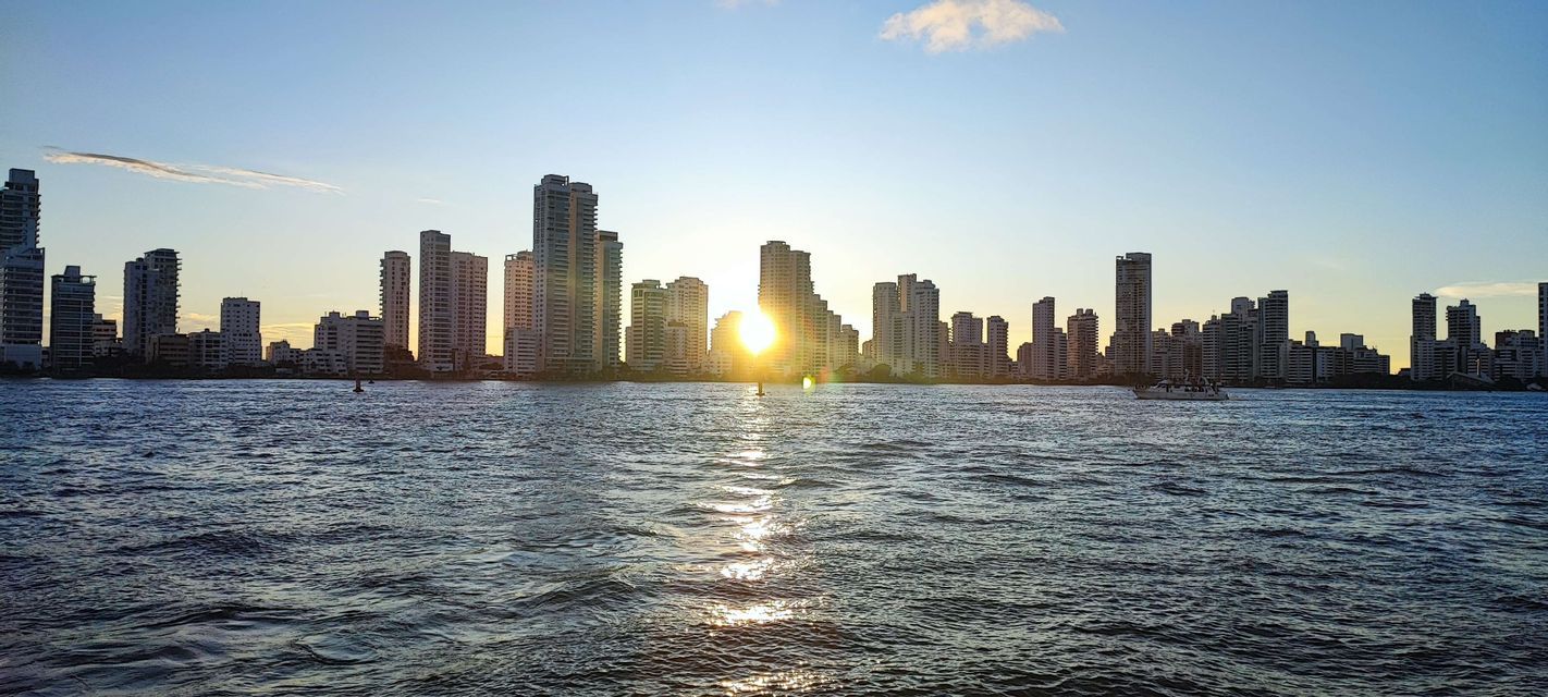 Eine Skyline hoher Gebäude, vom Wasser aus bei Sonnenuntergang gesehen, mit der Spiegelung der Sonne auf den Wellen.