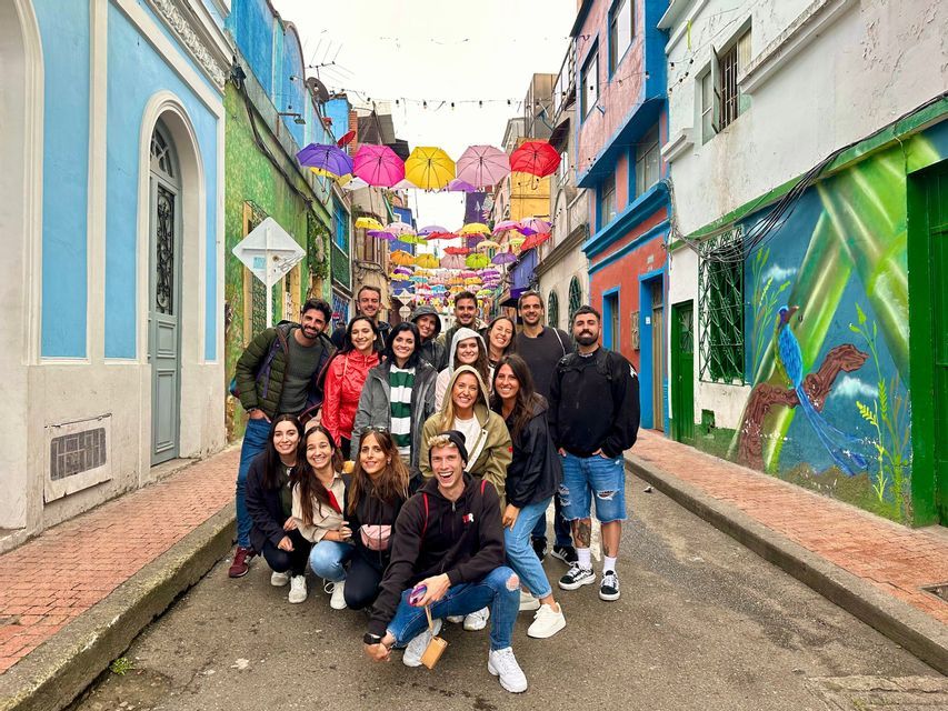 A WeRoad group trip poses for a photo on a colorful street under a canopy of hanging umbrellas.