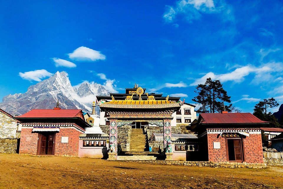 An ornate monastery with a golden-roofed portal stands in a courtyard beneath a massive snow-capped mountain.