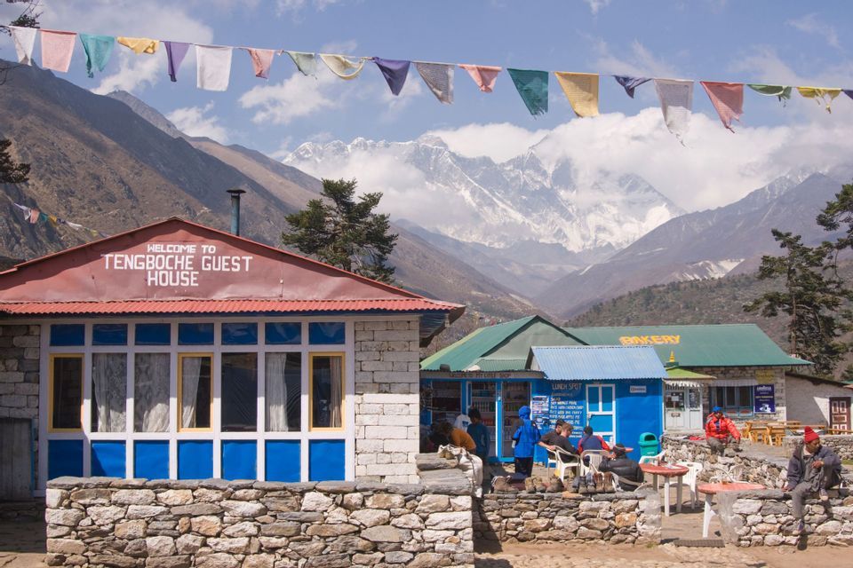 La Tengboche Guest House in un villaggio di montagna, con bandiere di preghiera e cime innevate sullo sfondo.