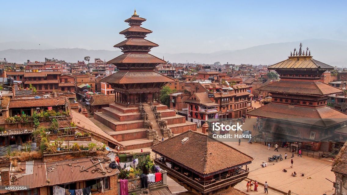Aerial view of a multi-tiered pagoda temple in a historic city with red brick buildings and distant hills.