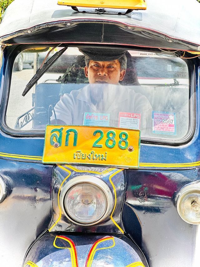 Ein Fahrer mit Mütze blickt aus dem Fahrersitz eines blauen Tuk-Tuks.