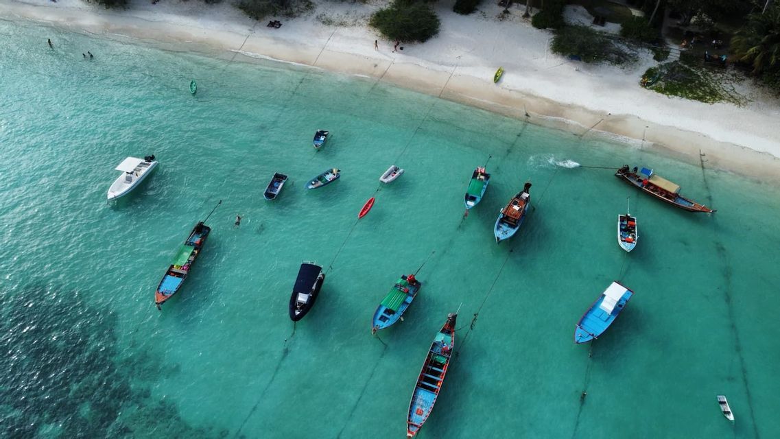 Luftaufnahme von bunten Booten, die in klarem türkisfarbenem Wasser nahe einem weißen Sandstrand ankern.