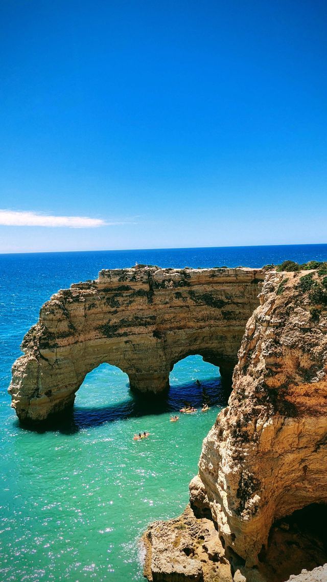 Un viaggio di gruppo WeRoad pagaia in kayak attraverso un doppio arco marino nell'oceano turchese in una giornata di sole.