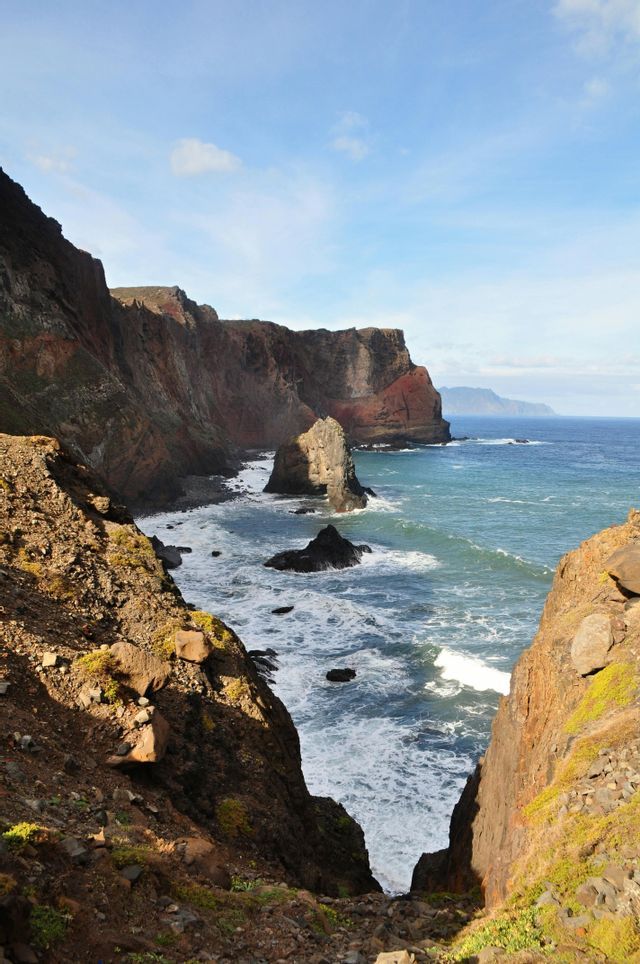 Alte scogliere rocciose e faraglioni lungo una costa con onde blu dell'oceano che si infrangono su di esse sotto un cielo limpido.