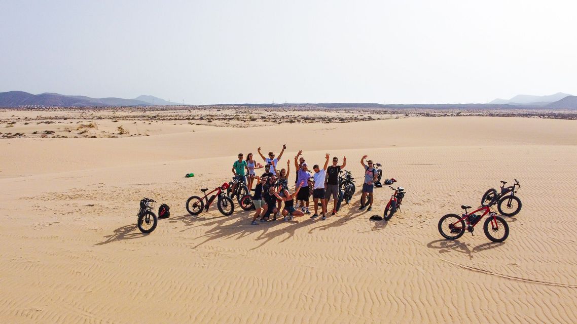 Un gruppo WeRoad posa con le loro fat bike sulle dune di sabbia in un paesaggio desertico.