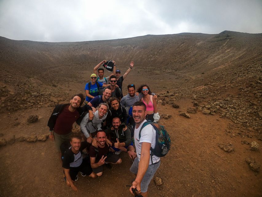 Un gruppo WeRoad si scatta un selfie all'interno di un grande cratere vulcanico roccioso sotto un cielo coperto.