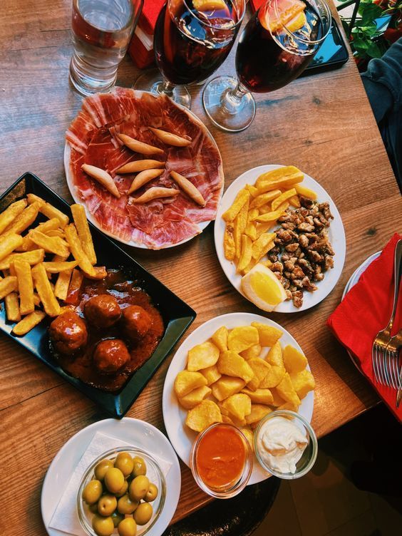 Una vista dall'alto di un tavolo di legno con vari piatti di tapas spagnole, inclusi jamón, polpette, patate e due bicchieri di sangria.