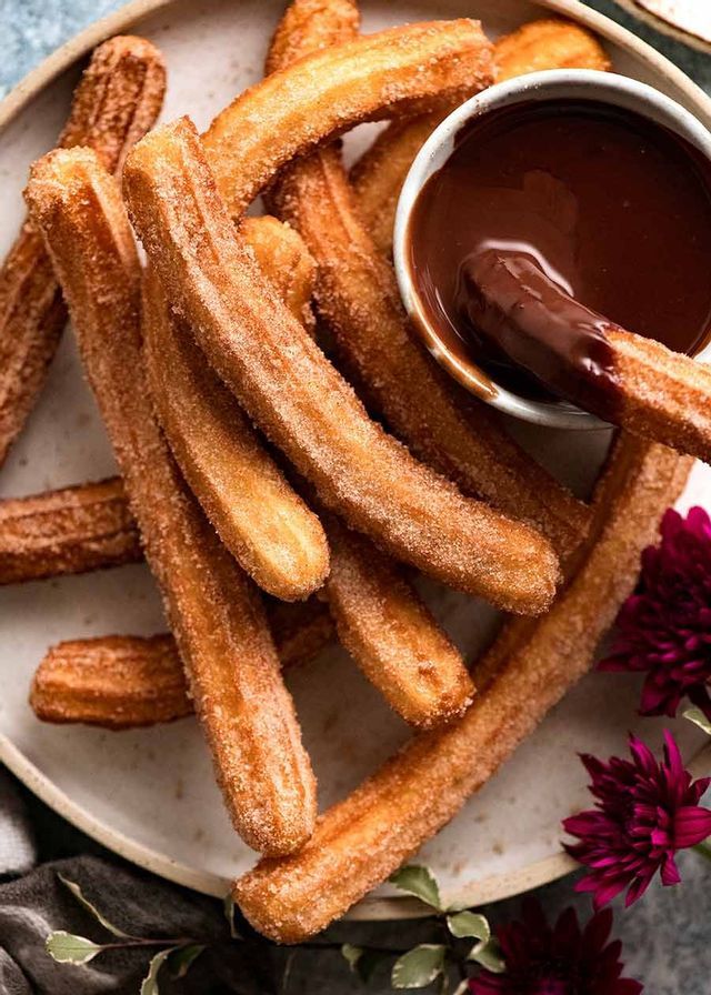 Un piatto di churros zuccherati con uno intinto in una ciotola di cioccolato fuso.