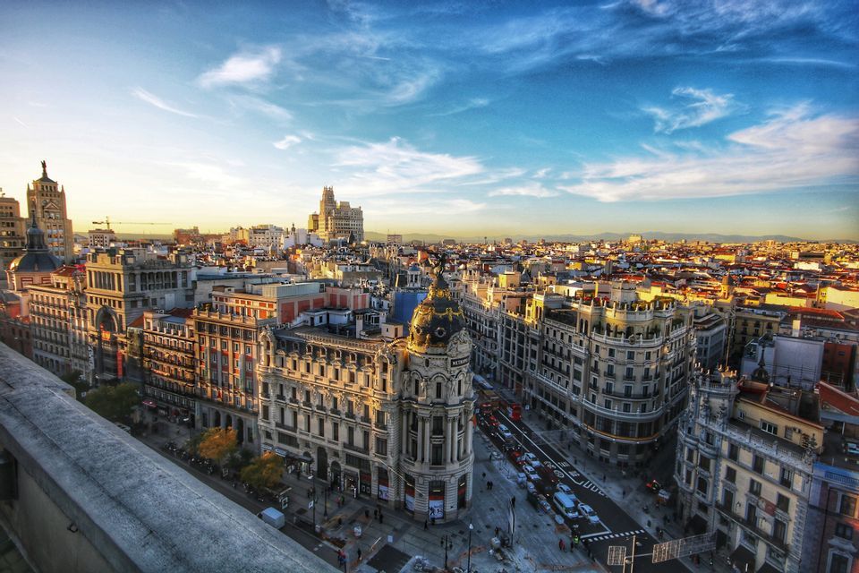 Vista aerea di una città europea al tramonto, con luce dorata su edifici ornati e strade trafficate.