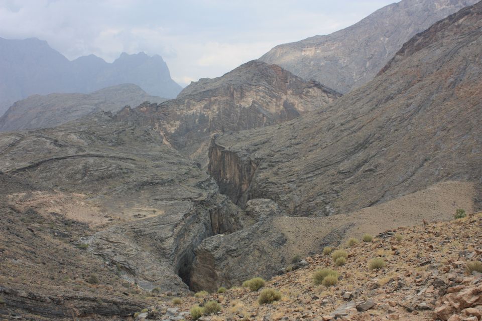 Una vista panoramica di una vasta catena montuosa rocciosa con un profondo canyon che la attraversa al centro, sotto un cielo coperto.