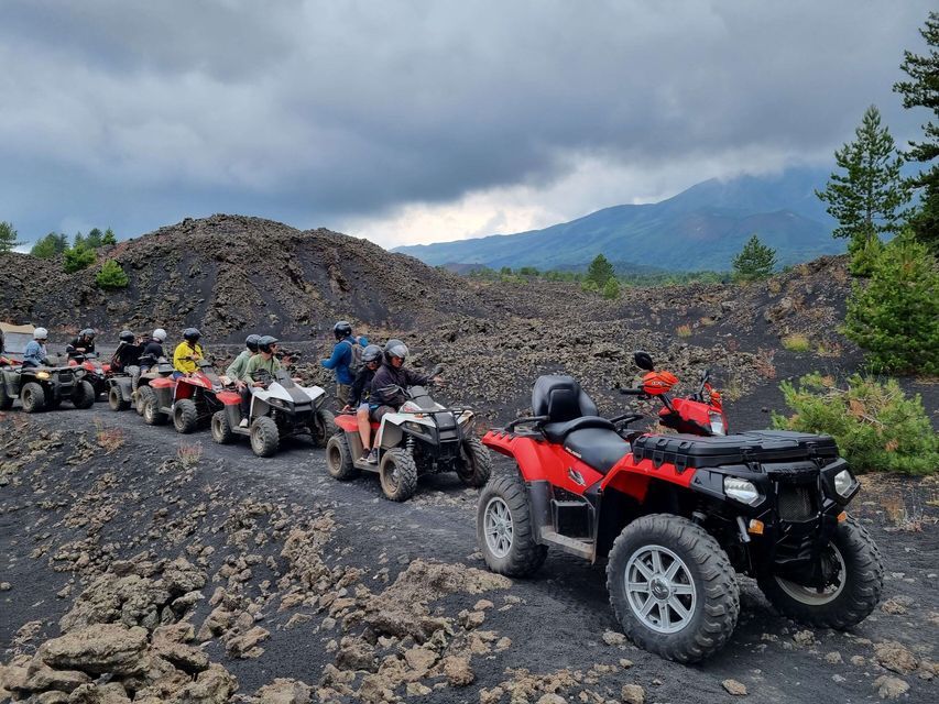 Un viaje en grupo de WeRoad en quads en fila a través de un paisaje volcánico rocoso con montañas al fondo.