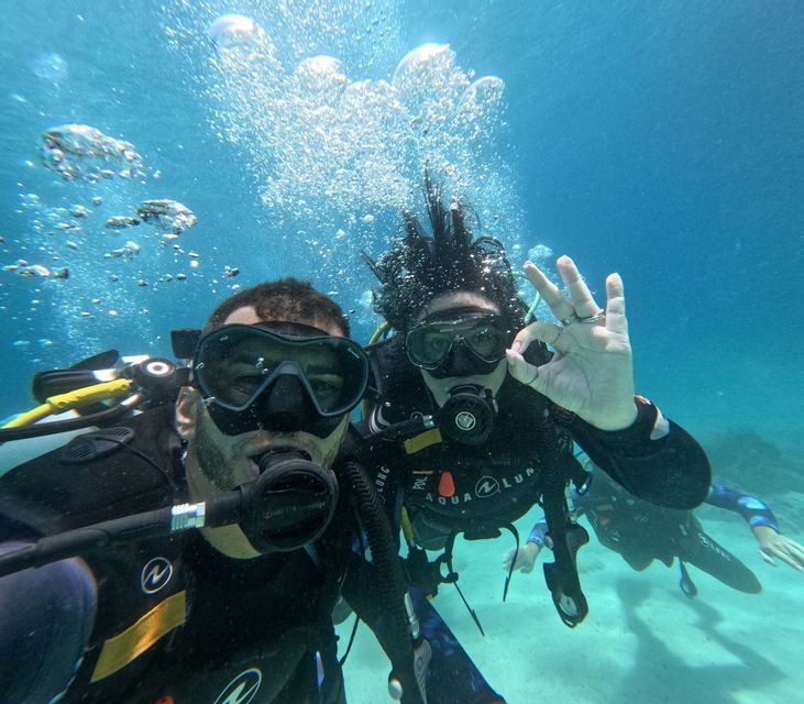 Dos viajeros de WeRoad se hacen una selfie subacuática mientras bucean, uno haciendo el gesto de OK.