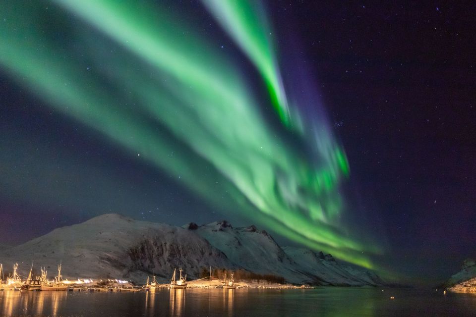 L'aurora boreale verde illumina il cielo notturno sopra le montagne innevate e un porto.