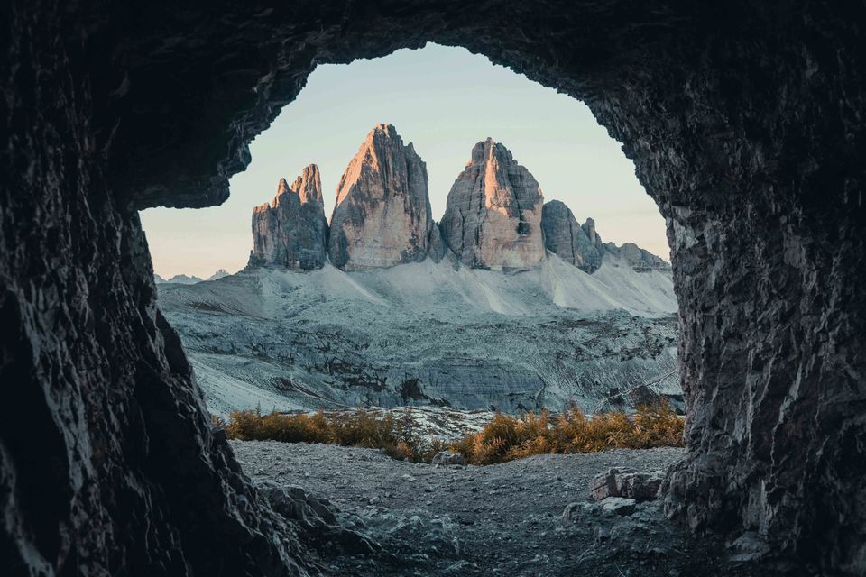 Blick auf sonnenbeschienene, zerklüftete Berggipfel aus einer dunklen Felshöhle, der die felsige Landschaft darunter umrahmt.