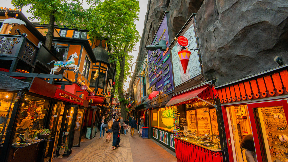 Personas paseando por una calle estrecha y pintoresca, con edificios coloridos y decorados y tiendas luminosas.