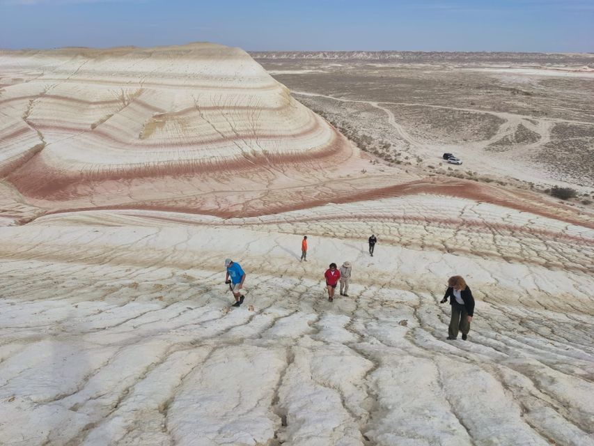Un grupo de WeRoad camina sobre tierra blanca agrietada frente a grandes colinas rayadas y coloridas bajo un cielo amplio.