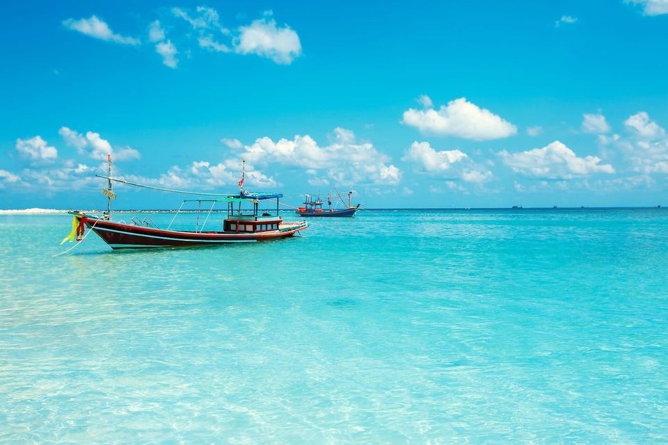 Two traditional wooden boats float on calm, turquoise ocean water under a bright blue sky with scattered white clouds.